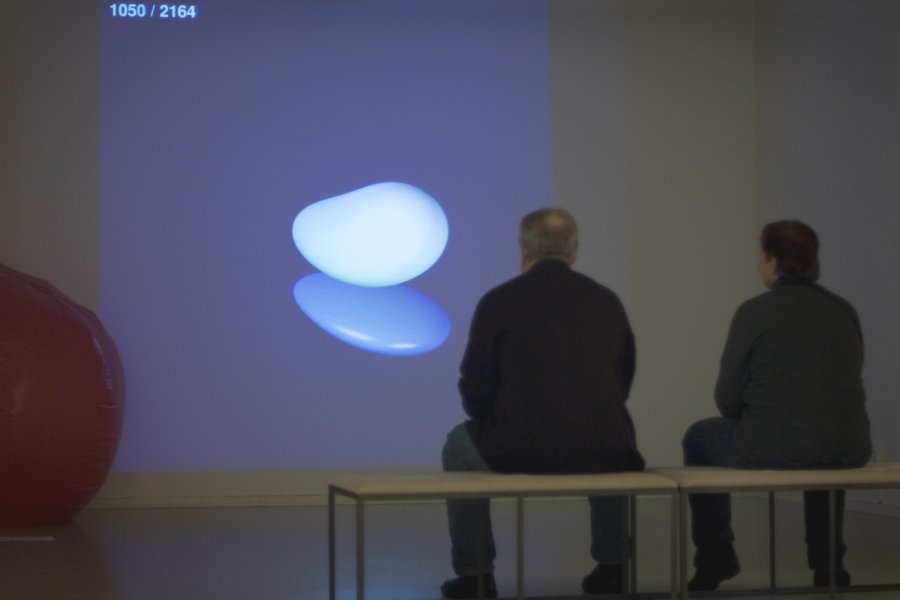 Two visitors watching the video of the evolving sculpture at the exhibition